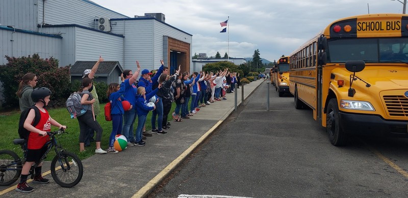 Staff wave goodbye to students as the leave on the last day of school